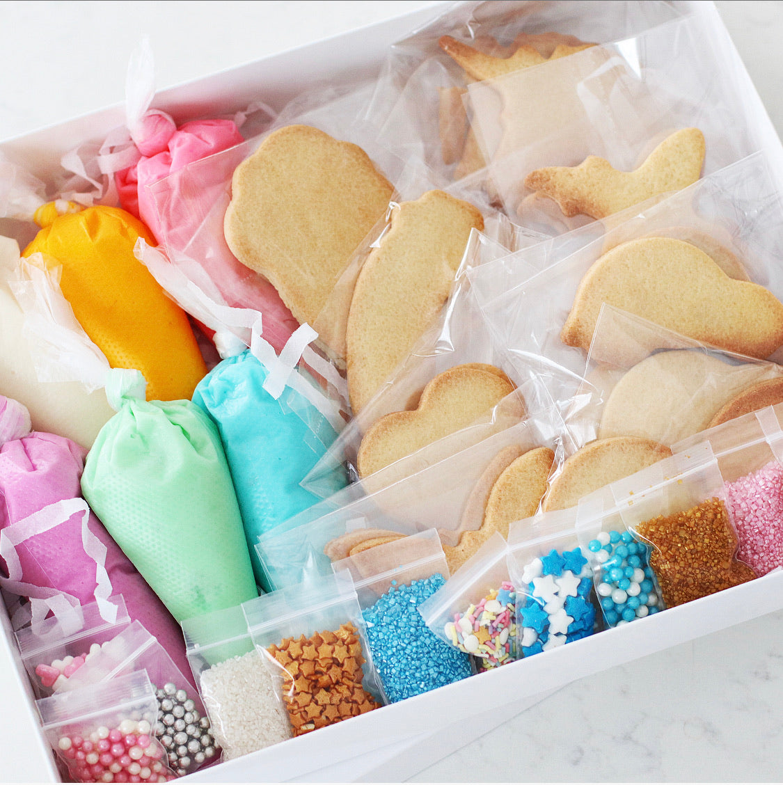 The Ultra-Mega DIY Cookie Kit - Includes 6 Piping bags, filled with ready to use icing in Blue, Purple, Pink, White, Yellow & Green.  10 Bags of sprinkles/decorations  20 Cookies, ready to decorate. Cookie shapes will include a mixed selection of all of our kits.